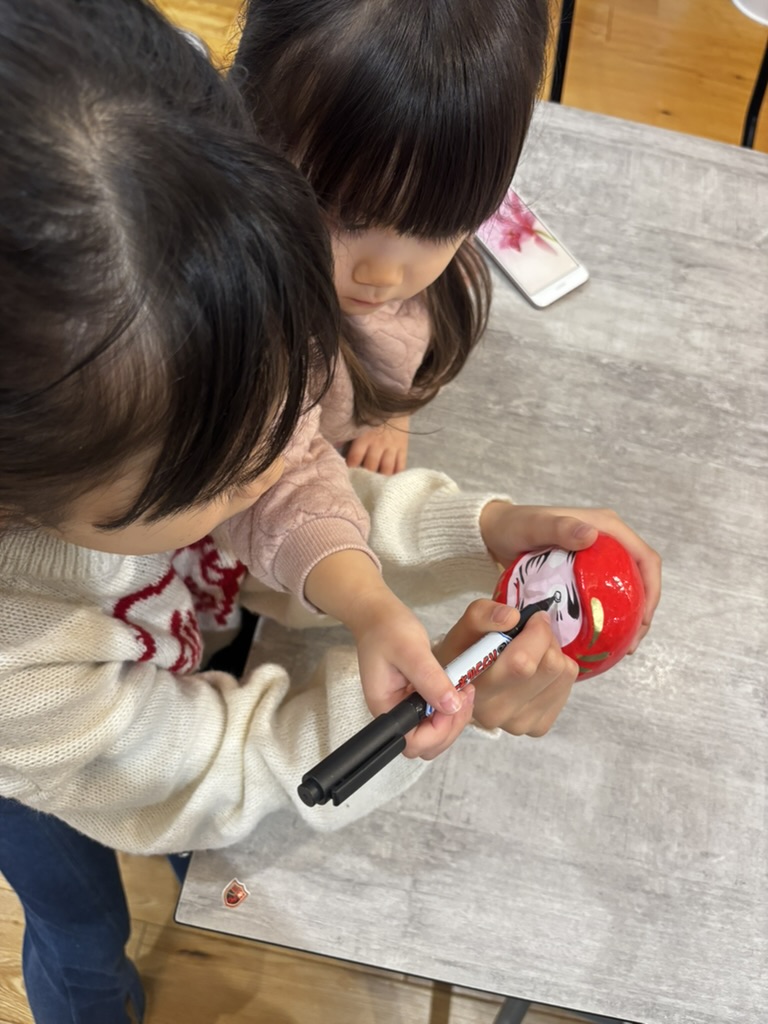 だるまに右目を描く娘二人の写真